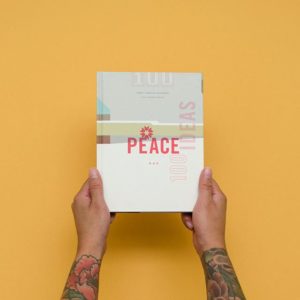 CDA's Peace 100 Ideas book being held over yellow backdrop