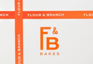 Branded packaging box with a debossed F&B monogram and branded red ribbons