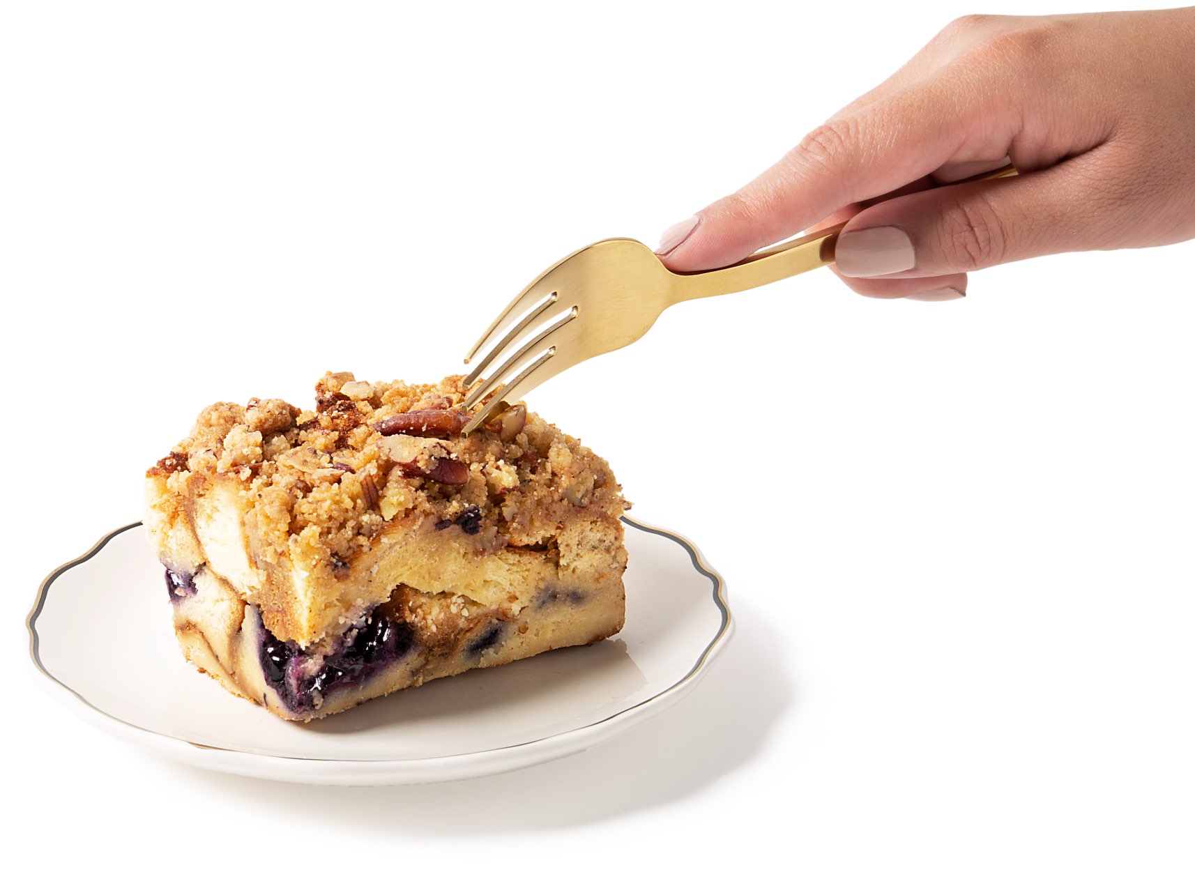 Product photography showing a hand with a fork hovering over a slice of Beshert French Toast on a gilded white plate