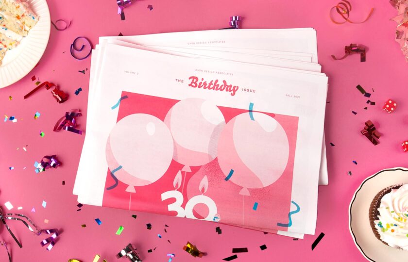 Cover of the Birthday Issue on a pink tablecloth surrounded by confetti and cake