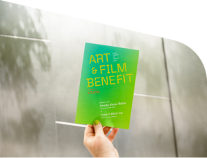 Photo of hand holding BAMPFA Art & Film Benefit event invite in front of building